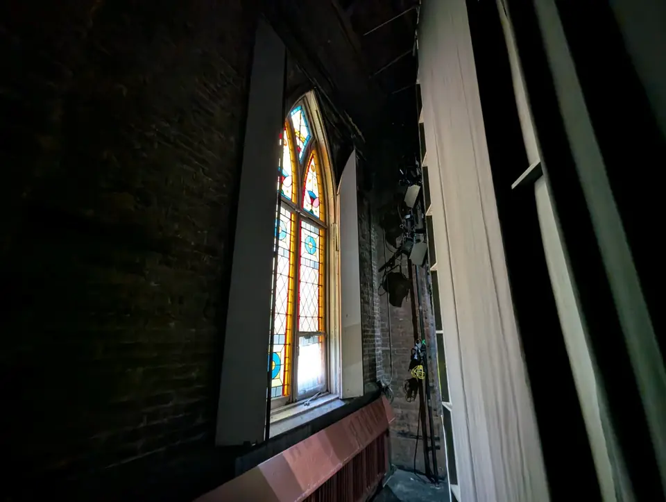 Daylight through a stained glass window backstage, beside the stage lights and curtains