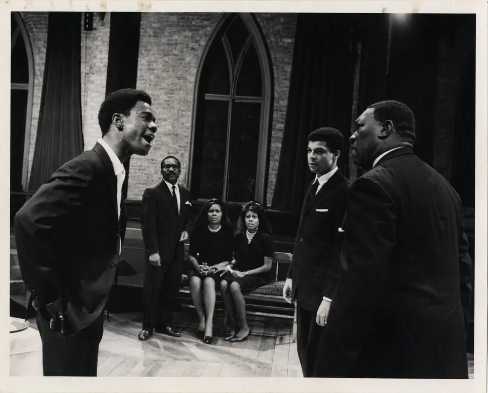 Six actors rehearse on the wooden floor of the sanctuary, its plaster stripped to bare brick, with a tall Gothic window and stage curtains behind them
