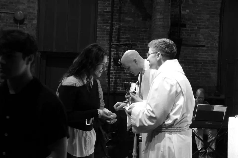 Communion: a woman smiles as she receives the bread from the priest, a server holding the chalice