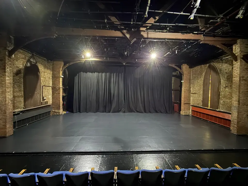 The empty stage from the front row, the black curtain closed between the old church’s brick piers